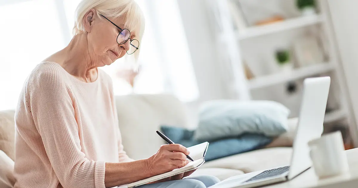 Woman writing something down while sitting on the couch at home.