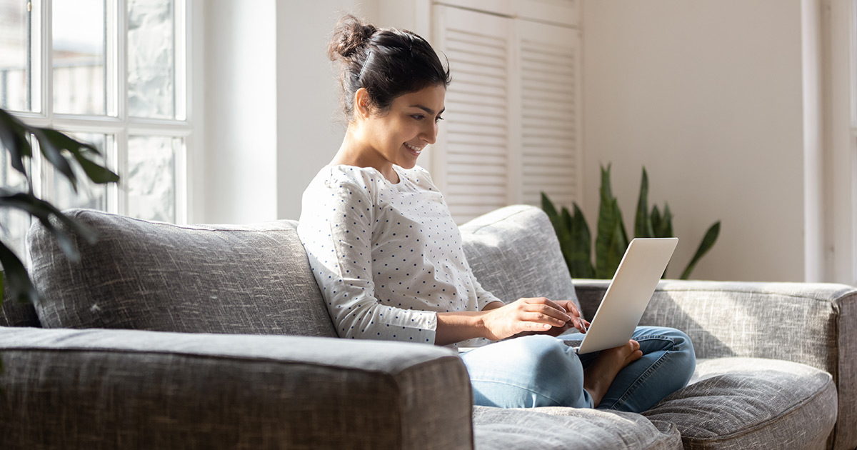 Femme assise sur son canapé tout en tapant sur un ordinateur portable.