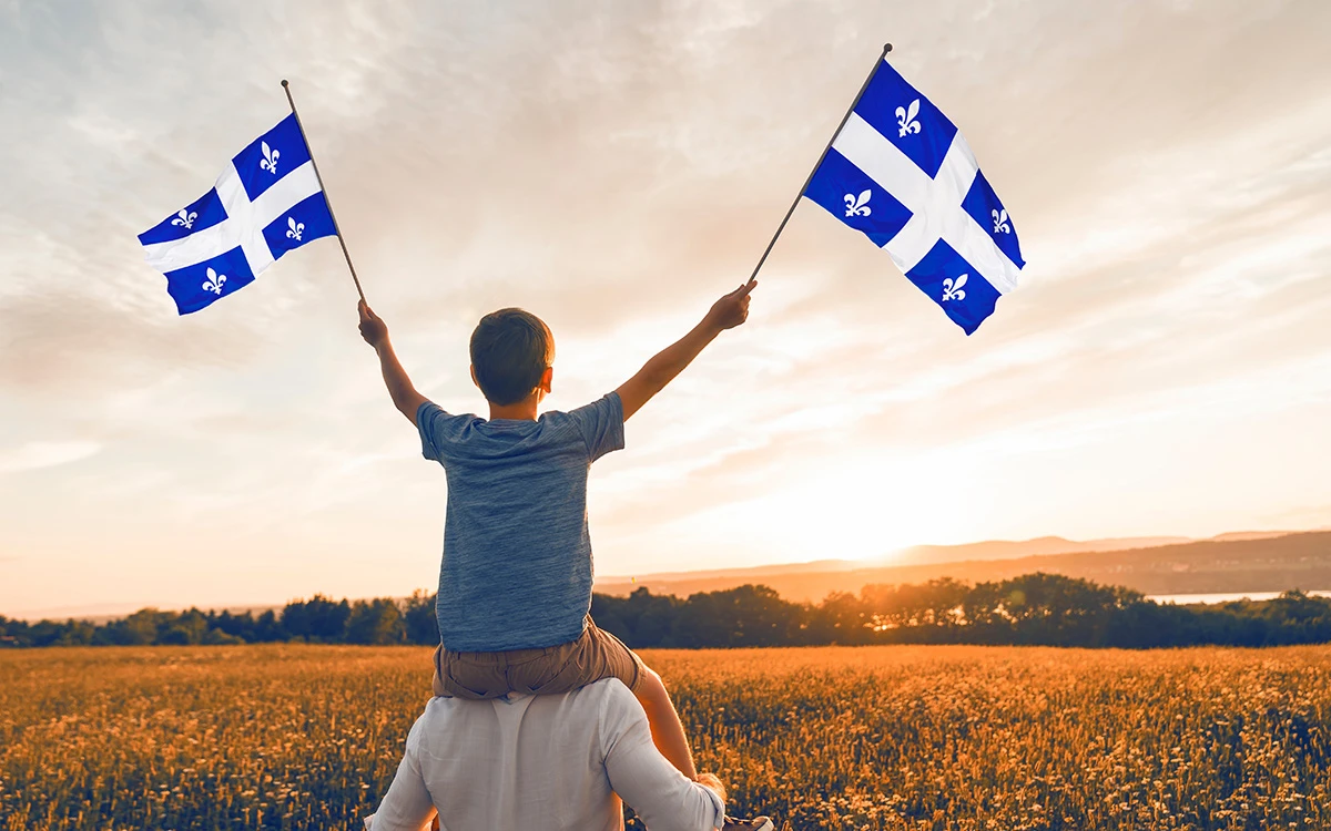  Garçon sur le dos d'un homme tenant deux drapeaux du Québec regardant un coucher de soleil